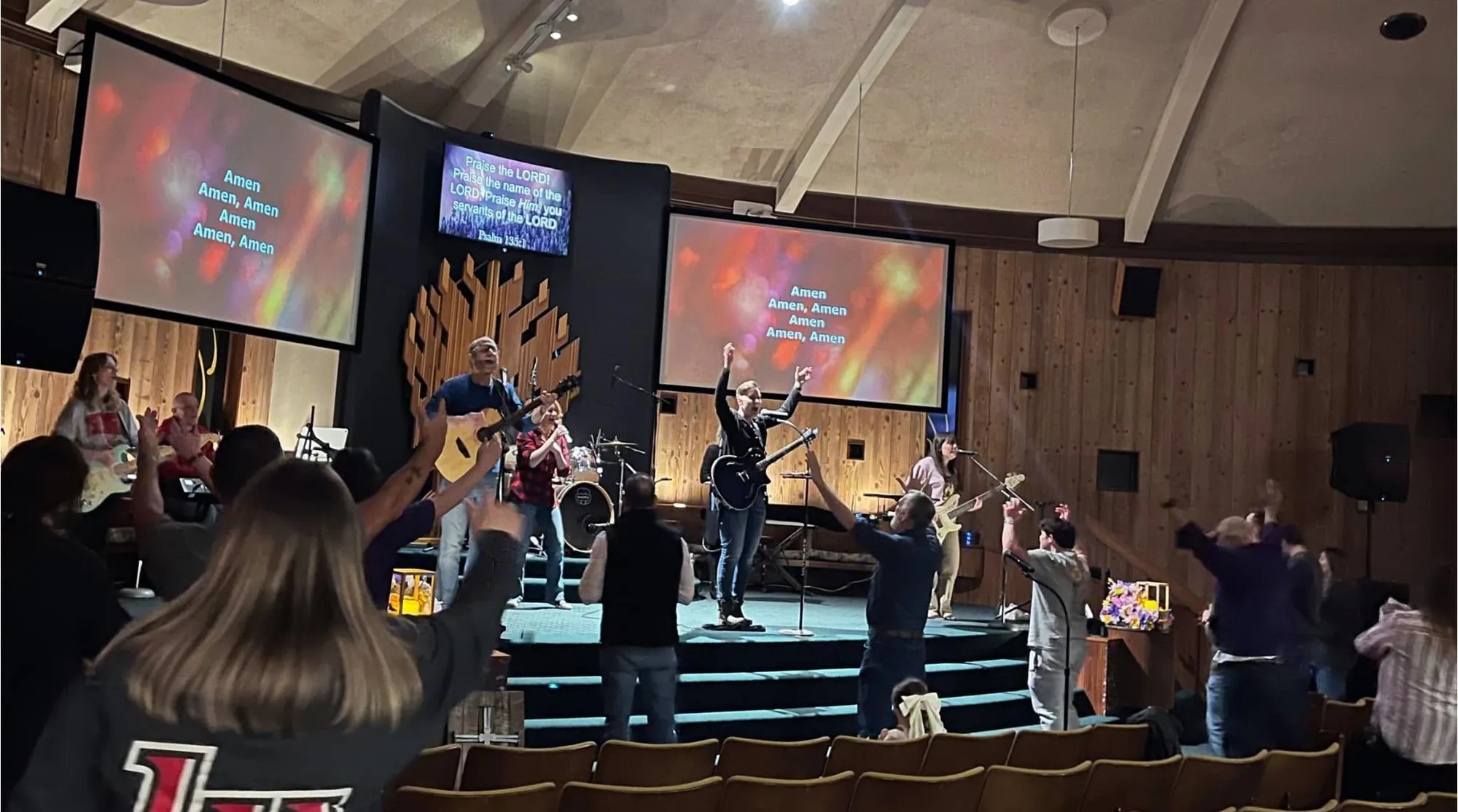 The Rush Church congregation raising their hands in worship, seen from behind facing the stage and band